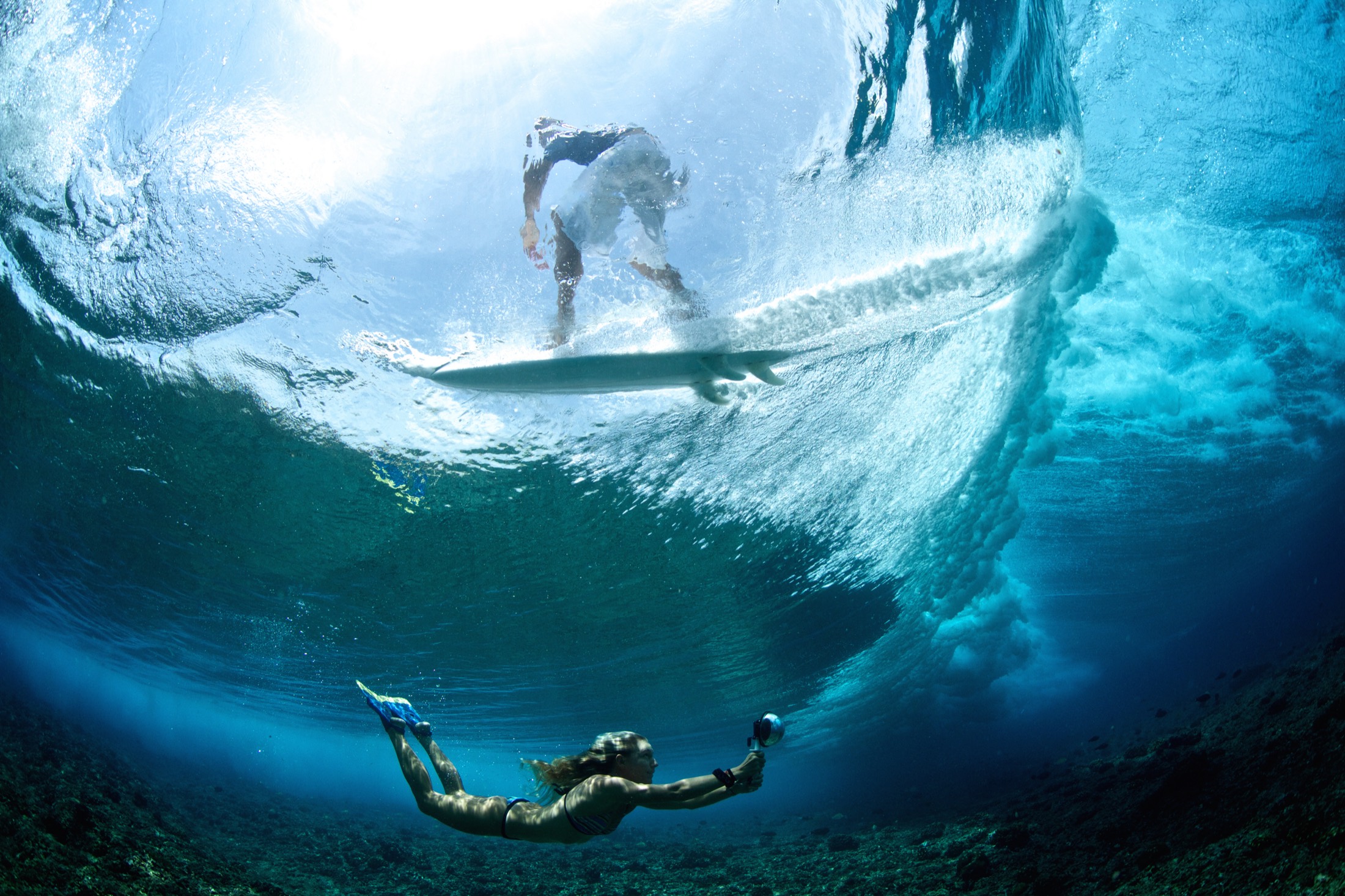 Underwater view of a surfer on a wave with a water photographer filming below