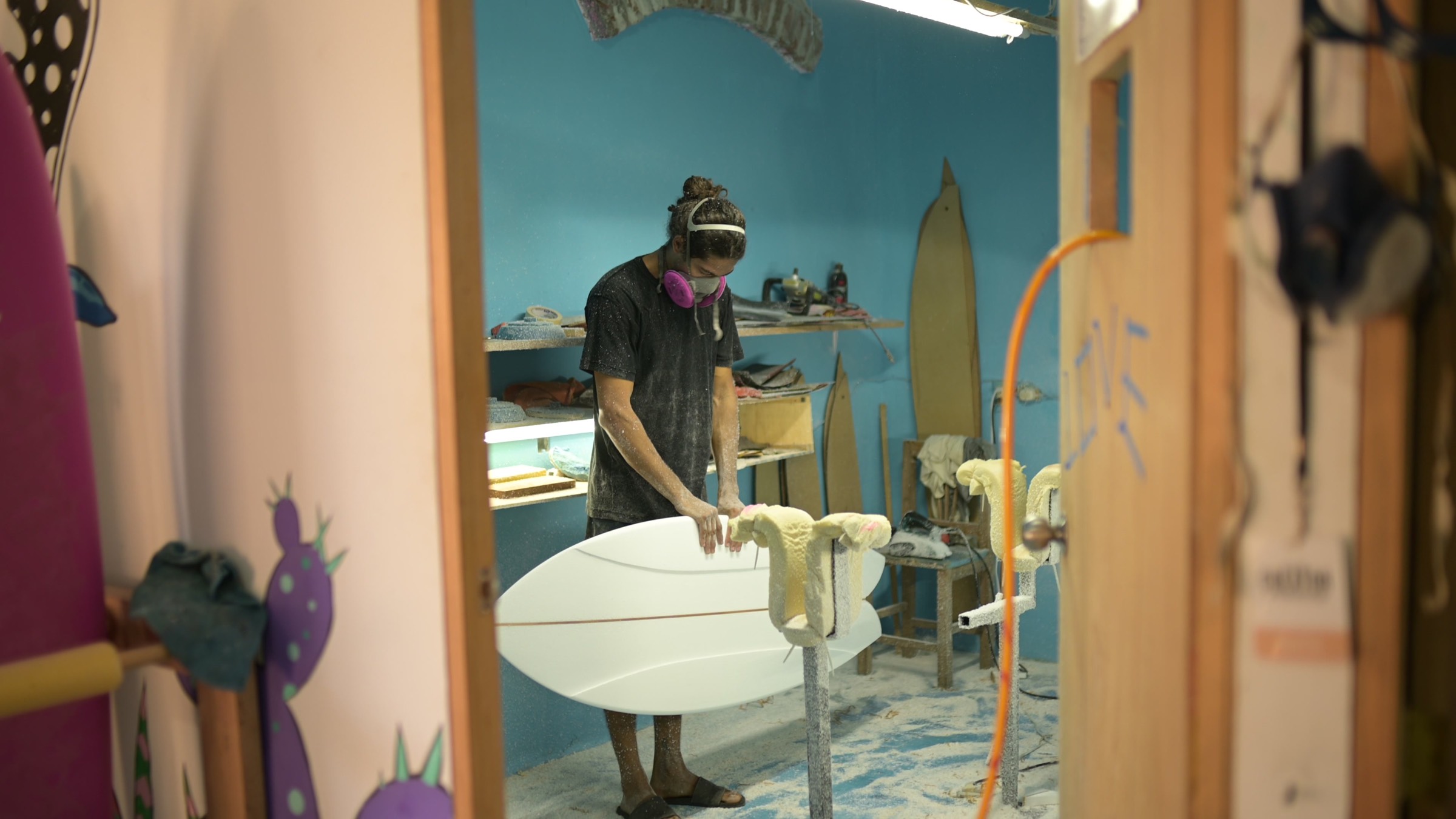 A shaper working a fresh surfboard blank in his shaping bay