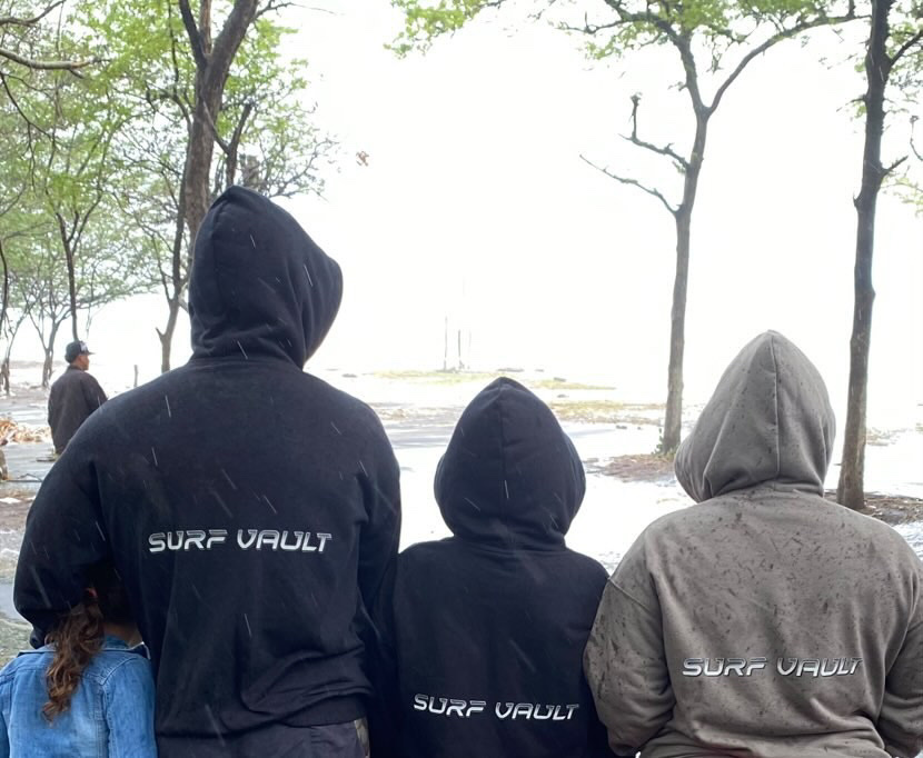 Tres personas con sudaderas de SurfVault mirando el agua